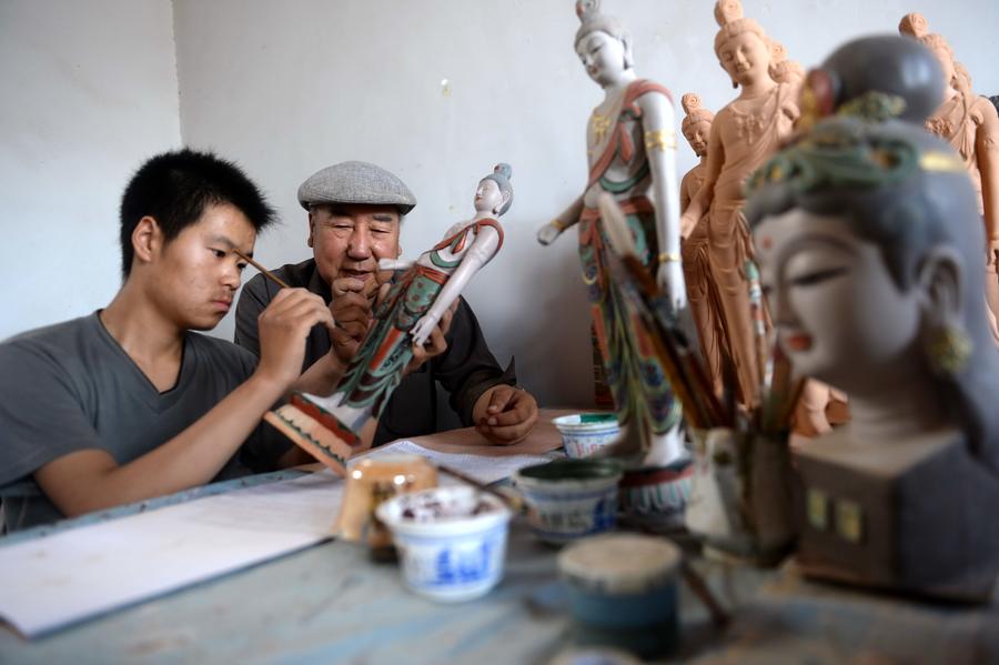 Lu Xueqin (à droite) enseigne à un élève comment peindre une sculpture en argile à l’Institut de Formation des Statues Peintes de Dunhuang, le 26 juin 2014.  