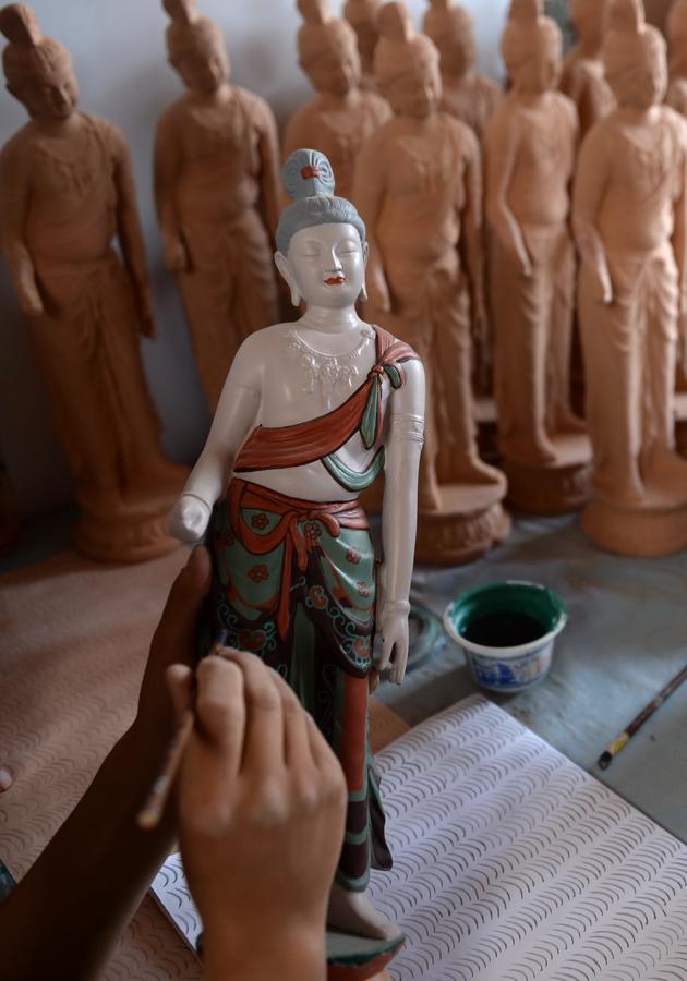 Un jeune artiste peint une sculpture en argile à l’Institut de Formation des Statues Peintes de Dunhuang, le 26 juin 2014.  