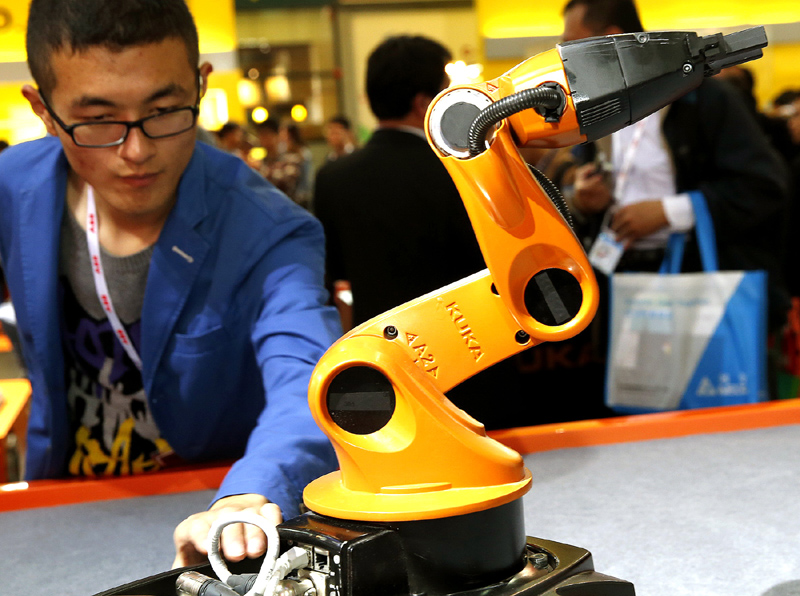 Un homme regarde un robot multifonctions conçu par la société de robotique allemande KUKA, exposé pendant le 16e Salon international de l'industrie de Chine à Shanghai, le 4 novembre 2014. [Photo/Xinhua]