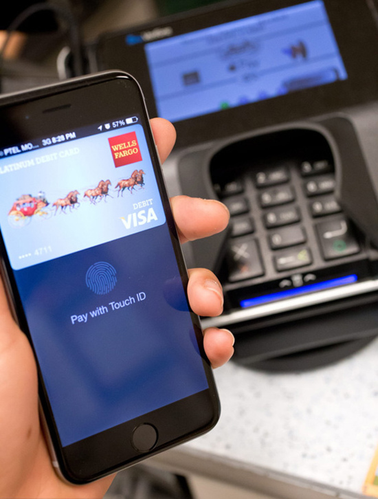 Un client paie avec Apple Pay sur un terminal NFC, en avril 2015. Le capteur Touch ID dans le bouton d'accueil authentifie l'empreinte digitale du client pour confirmer la transaction. [Photo / IC]