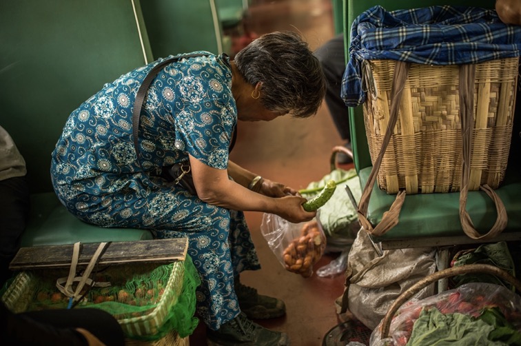 Avant de démarrer les ventes, une femme âgée profite d’une pause dans le train pour prendre son petit déjeuner, au menu un concombre et du pain cuit.