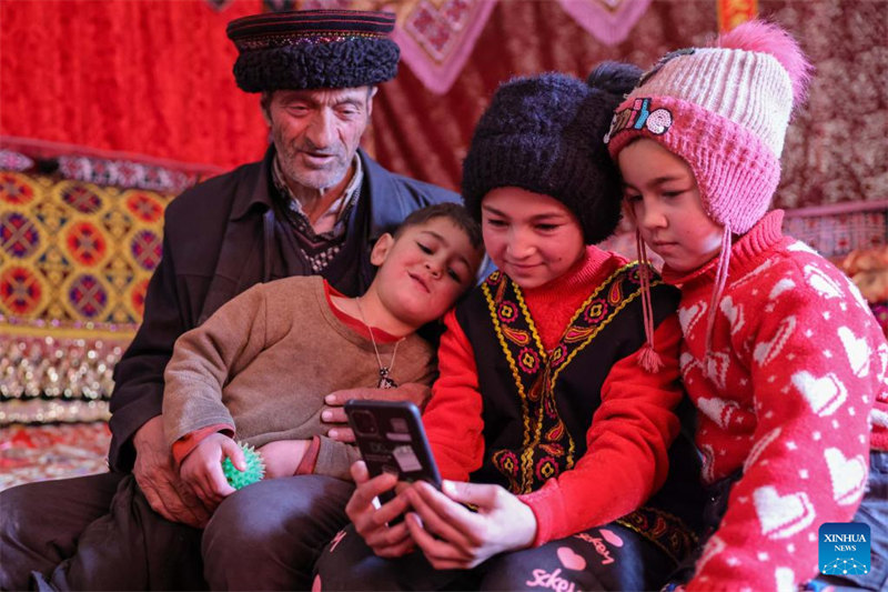 Des enfants regardent des vidéos sur un téléphone portable avec un membre de leur famille dans le village de Rasekam du district autonome Tadjik de Taxkorgan, dans la région autonome ouïghoure du Xinjiang (nord-ouest de la Chine), le 24 février 2022. (Photo / Xinhua)