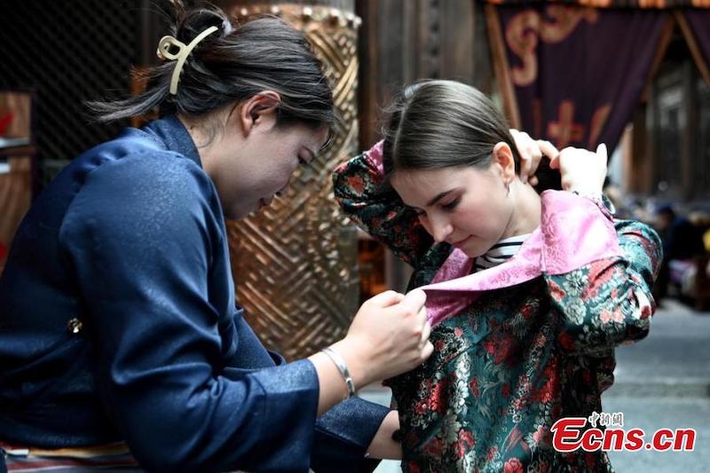 Un membre du personnel aide une jeune femme à essayer des vêtements tibétains lors d'un événement organisé dans la vieille ville de Dukezong, dans le comté de Shangri-la dans la province du Yunnan (sud-ouest de la Chine), le 26 juin 2023. (Li Jiaxian / China News Service)