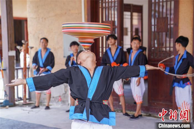 Un membre du peuple Baiku Yao montre aux touristes comment faire tourner un gyroscope sur leur tête. (Chen Guanyin / China News Service)