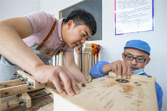 Wang Sheng (à gauche) demande à un ouvrier d'installer la caisse de résonance d'une vièle à tête de cheval. (Buyandelger / le Quotidien du Peuple en ligne)