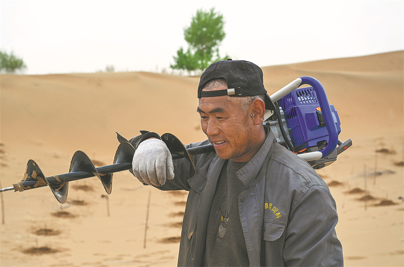 Un membre de l'équipe porte un semoir sur son épaule alors qu'il se dirige vers la zone de plantation. (Liu Lei / Xinhua)