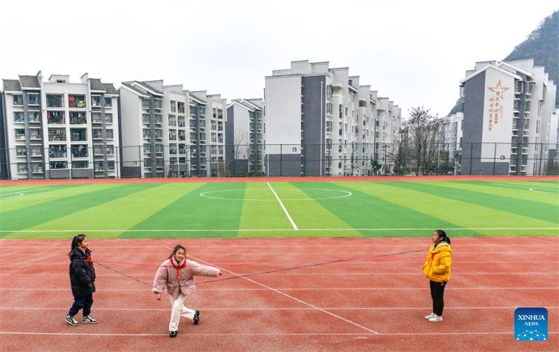 Ji Xue (au centre) joue avec ses camarades à l'école, avec leurs nouvelles maisons à l'arrière, dans le district de Xixiu, à Anshun, dans la province du Guizhou (sud-ouest de la Chine), le 22 décembre 2023. (Yang Wenbin / Xinhua)