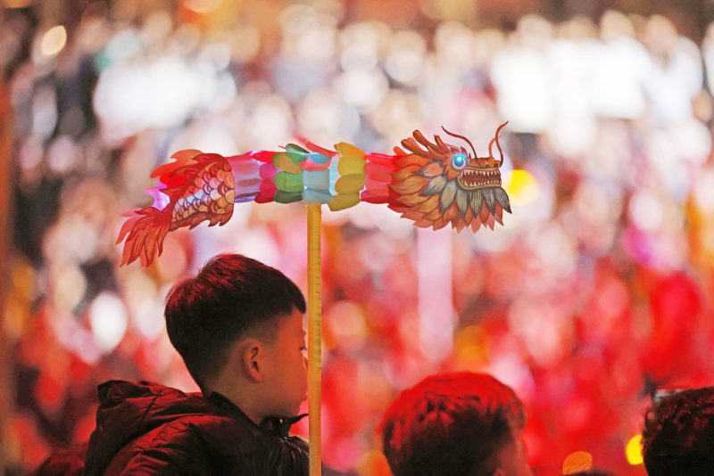 Un jeune garçon tenant une lanterne en forme de dragon regarde un spectacle lors d