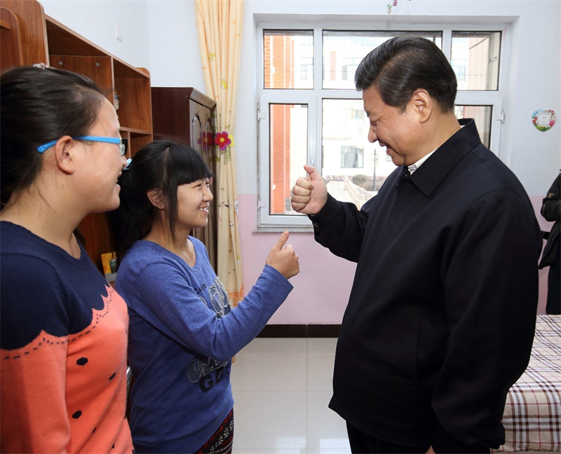 Xi Jinping apprend le mot « merci » en langue des signes avec Wang Yani (deuxième à gauche), une jeune fille sourde-muette, et de Yan Zhijing, une de ses camarades qui « est rentrée chez elle » pendant les vacances, dans le dortoir de l'Institut de protection de l'enfance de Hohhot, capitale de la région autonome de Mongolie intérieure (nord de la Chine), le 28 janvier 2014. (Photo / Lan Hongguang)