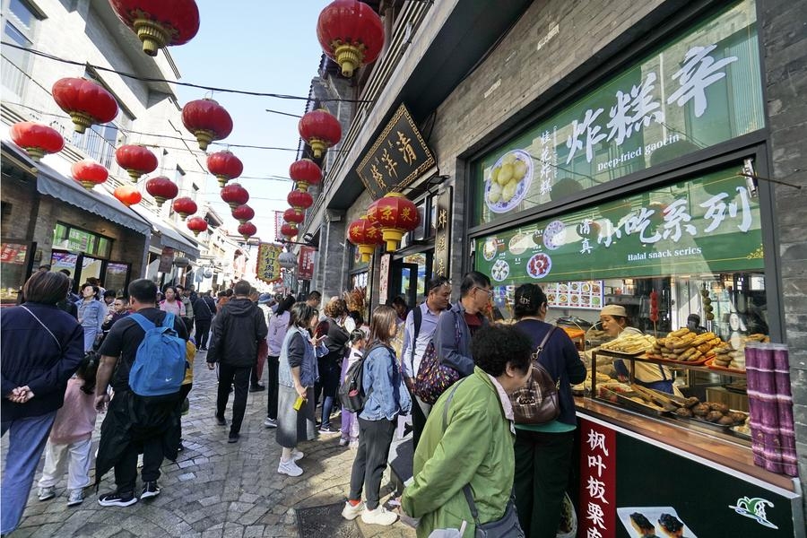 Des touristes dégustent de la nourriture dans la rue piétonne Qianmen à Beijing, capitale de la Chine, le 7 octobre 2024. (Photo : Li Xin)