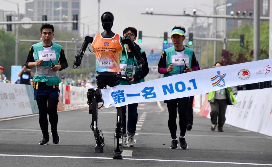 Le participant robotique « Tiangong Ultra » (2e à gauche) franchit la ligne d'arrivée tandis que des ingénieurs courent à ses côtés lors du semi-marathon E-Town de Beijing et du semi-marathon de robots humanoïdes dans la zone de développement économique et technologique de Beijing, dans le sud-est de la capitale chinoise, le 19 avril 2025. (Photo / Xinhua)