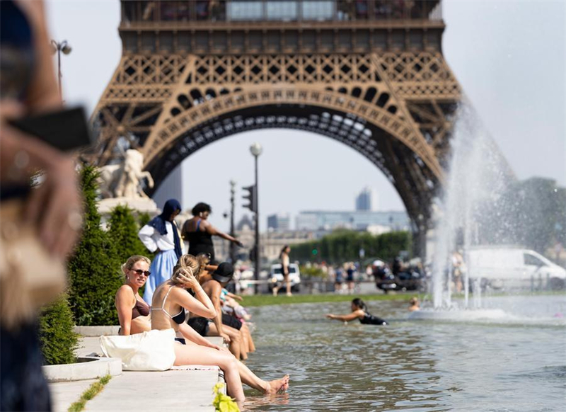 Des gens viennent se rafraîchir et se détendre près d'une fontaine devant la tour Eiffel à Paris, en France, le 23 juin 2026. (Wu Huiwo/Xinhua)