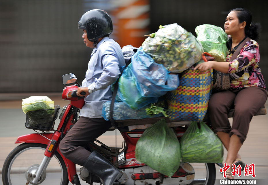 A Phnom Penh, au Cambodge, un homme conduit une moto chargée de plus de dix sacs de légumes. Ce qui est étonnant, c'est cette femme à l'arrière qui semble confortablement assise.