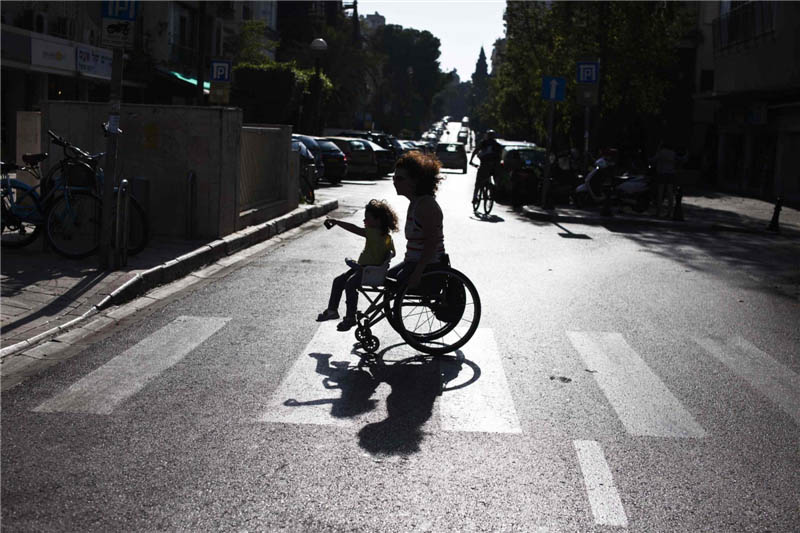 Pascale Bercovitch porte sa fille, Mica, âgée de 3 ans, sur son fauteuil roulant alors qu'elles traversent une route près de leur maison à Tel-Aviv, le 16 mai 2012. Mme Bercovitch, 44 ans, qui a perdu ses jambes dans un accident de train en France en 1984, a représenté Israël lors des Jeux paralympiques de Londres dans l’épreuve de cyclisme à main.