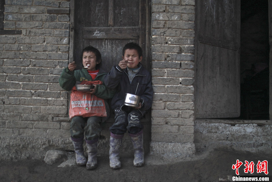 Deux enfants déjeunent devant la porte de leur salle de classe. Leur déjeune n'est qu'un peu de pomme de terre et une soupe de chou fermenté, cuites dans la petite cuisine du professeur Tao Jinjun. (Chinanews/Feng Zhonghao)