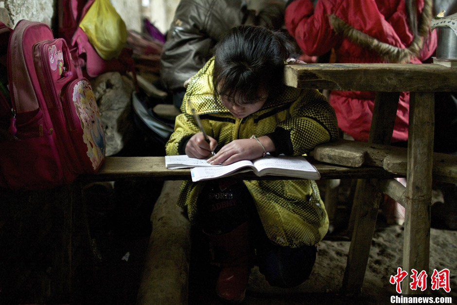 La seule école primaire du village Laodong se trouve dans une maison de deux pièces. A cause de l'état miteux de la maison, l'école n'est pas intégrée dans le réseau d'alimentation d'électricité. Ainsi, les élèves suivent des cours à l'aide de l'éclairage naturel. Sur cette photo, une fille s'agenouille pour profiter des lumières naturelles pour lire son texte. (Chinanews/Feng Zhonghao)