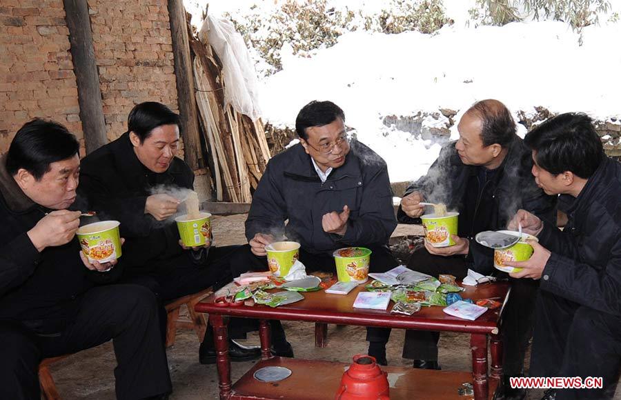 Photo d'archive prise le 31 janvier 2008 montrant Li Keqiang (3e à gauche) discutant des opérations de secours tout en prenant un simple repas de nouilles instantanées après avoir constaté les dégâts et rendu visite aux sinistrés du village de Ziyun du district de Xuanhan de la province du Sichuan (sud-ouest), en Chine.