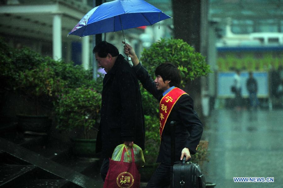 Le 26 janvier 2013, un bénévole tient un parapluie pour aider un passager à la gare de Nanning, la capitale de la Région autonome Zhuang du Guangxi. (Xinhua/Huang Xiaobang)