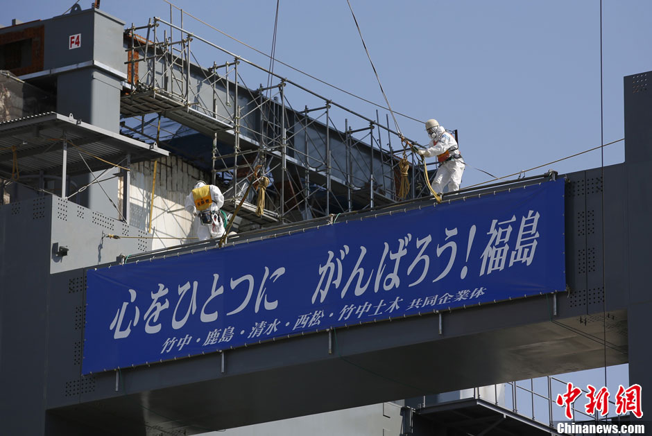Sur un bâtiment de stockage des barres nucléaires en cours de reconstruction, avec la mention, « déclassement » figure le slogan « Tous ensemble d’un même cœur, courage Fukushima ! ».
