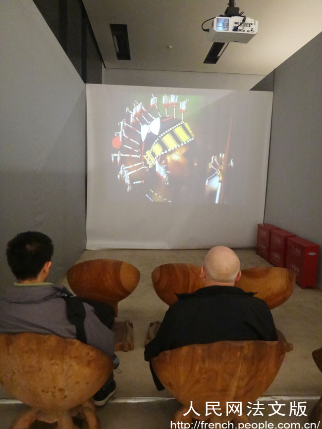 Dans un coin de la salle d'exposition, des visiteurs regardent une vidéo de la présentation de sculptures africaines. 