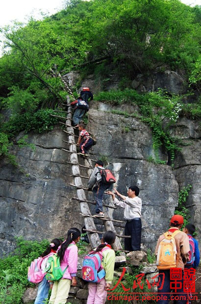 Dans le Comté de Ganluo, dans la Province du Sichuan, les enseignants aident les enfants à passer un par un sur une échelle branlante en bois. Leur école est située à une altitude de 2 800 mètres sur une falaise, et cette fragile échelle en bois est devenue pour eux leur seul moyen de transport.