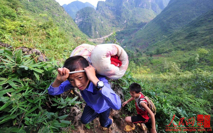 Dans le Comté autonome Yao de Dahua, dans la Province du Guangxi, deux élèves empruntent un sentier de montagne accidenté vers l'école. Les écoles primaires rurales locales sont en général situées très loin du domicile des élèves, et la majorité des élèves vivent donc sur le campus, et ne rentrent chez eux que pendant les longs congés.