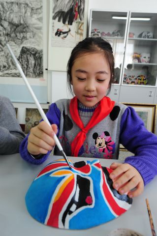 Le 26 mars, une écolière colorie un masque de l’opéra de Beijing à l’école primaire Xiaoxiang de Yantai.