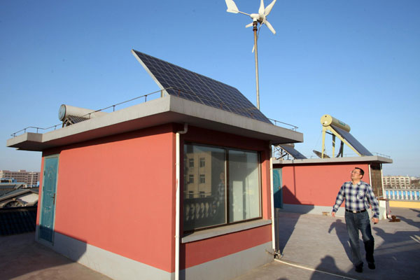 Dong Qiang, qui a demandé une autorisation pour vendre de l'électricité produite de façon indépendante à Tianjin, inspecte les grilles des panneaux d'énergie solaire et éolienne installés sur son toit à Tianjin, le 6 avril 2013. [Photo / Xinhua]