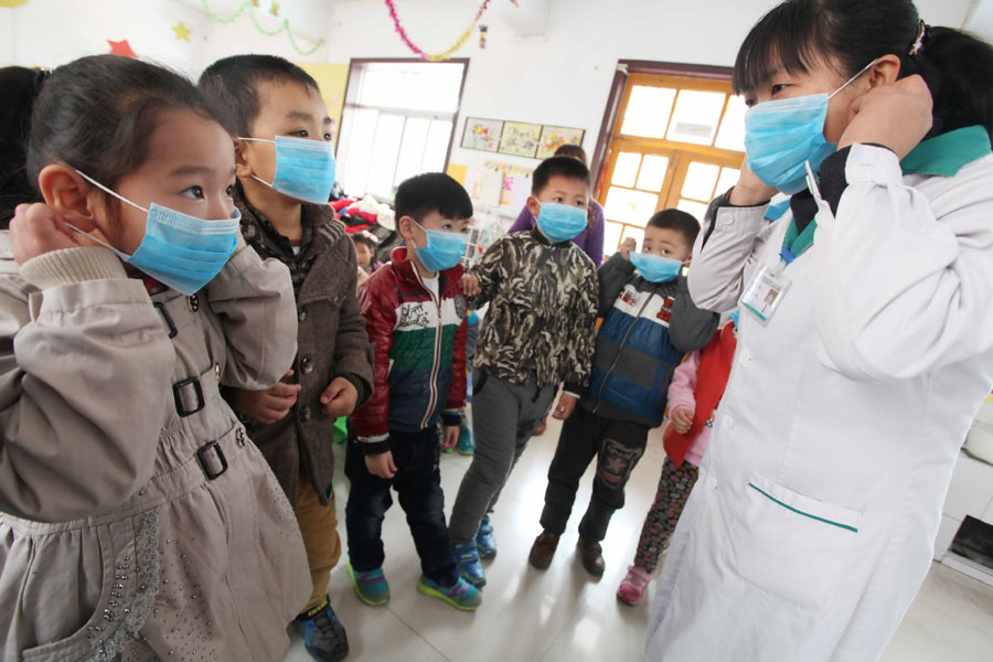 Un employé des services médicaux d'une communauté montre aux élèves comment porter des masques pour prévenir la grippe aviaire, dans la ville de Weifang, dans la Province du Shandong, dans l'Est de la Chine, le 8 avril 2013. [Photo Zhang Chi / Asianewsphoto]