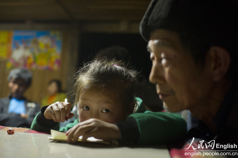 Le 11 avril 2013, la petite soeur de Yu Qiyun fait ses devoirs à côté de leur grand-père. (Photo : People's Daily Online)