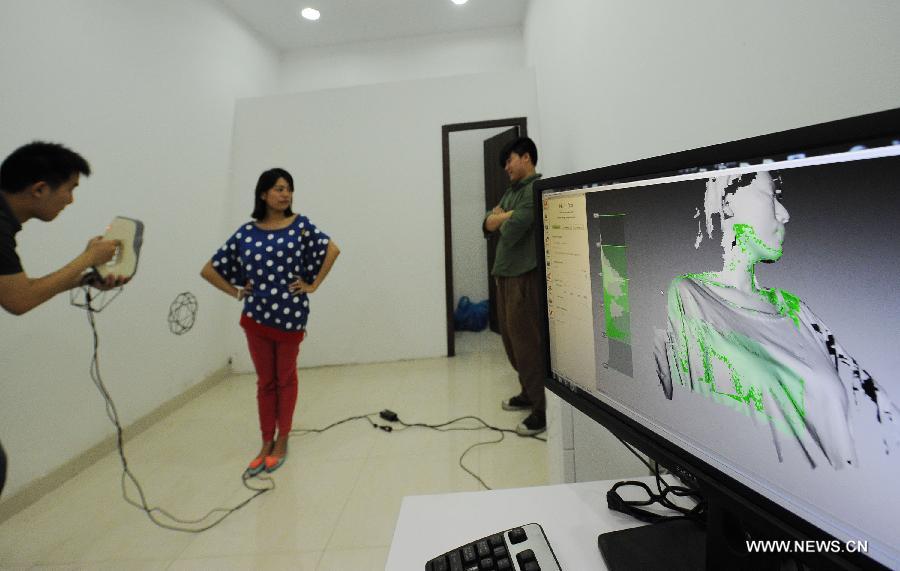 Un membre du personnel de la boutique scanne un jeune couple pour faire des figurines imprimées en 3D dans une boutique d'impression 3D qui vient d'ouvrir dans la municipalité de Chongqing, dans le Sud de la Chine, le 3 juin 2013. [Photo / Xinhua]