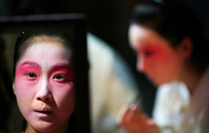 Une artiste se regarde dans un miroir, alors qu'elle applique son maquillage avant une avant-première d'un spectacle d'Opéra de Pékin réservée aux médias, au musée des textiles de Shanghai, le 8 juin 2013.