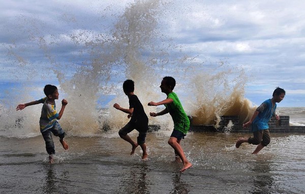 Des enfants jouent avec l'eau alors qu'une vague énorme atteint le rivage dans le village de Leshan dans la ville de Fangchenggang, dans la Région Autonome Zhuang du Guangxi, dans le Sud de la Chine, le 23 juin 2013. La tempête tropicale Bebinca a apporté de fortes pluies dans le Guangxi. [Photo / Xinhua]