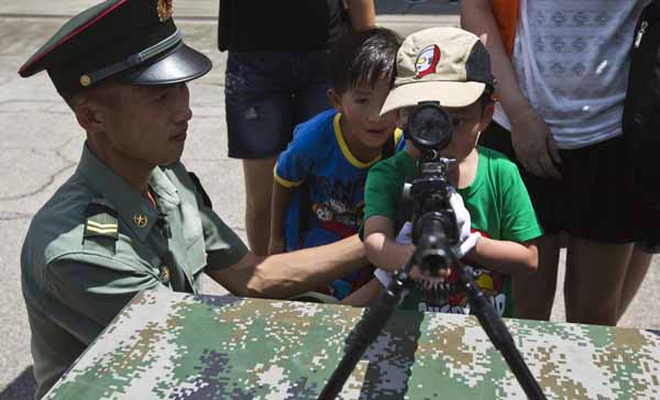 Un jeune garçon regarde à travers la lunette d'un fusil à côté d'un soldat de l’Armée de Populaire de Libération (APL) lors d'une journée portes ouvertes à la caserne Shek Kong à Hong Kong le 30 juin 2013. [Photo / agences]