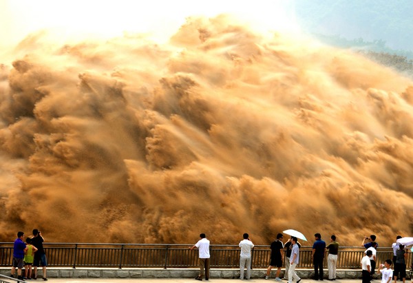Des touristes regardent l'eau qui jaillit du réservoir de Xiaolangdi sur le Fleuve Jaune, au cours d'une opération de nettoyage de sable à Luoyang, dans la Province du Henan, dans le Centre de la Chine, le 7 juillet 2013. L'opération en cours, qui a eu lieu vendredi, se fait en évacuant l'eau à un volume de 2 600 mètres cubes par seconde depuis le réservoir afin d’évacuer les sédiments présents dans le Fleuve Jaune, le deuxième plus long cours d'eau de Chine. Les courants rapides emportent des tonnes de sable vers la mer. Le Fleuve Jaune est encombré par une quantité croissante de boue et de sable. Chaque année, le lit de la rivière monte à mesure que les dépôts de limon s'accumulent, ce qui ralentit l'écoulement de l'eau dans le cours inférieur. [Miao Qiunao / Asianewsphoto]