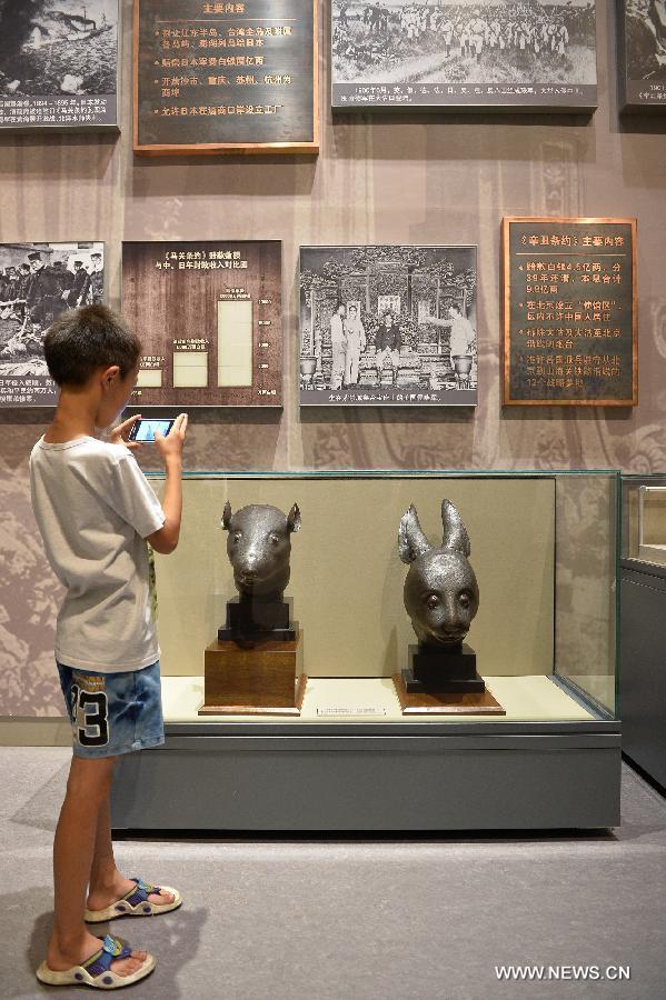 Un enfant prend en photo les têtes en bronze du rat et du lapin, données par la famille française Pinault en avril, exposées au Musée National de Chine à Beijing, capitale de la Chine, le 18 juillet 2013. [Photo / Xinhua]