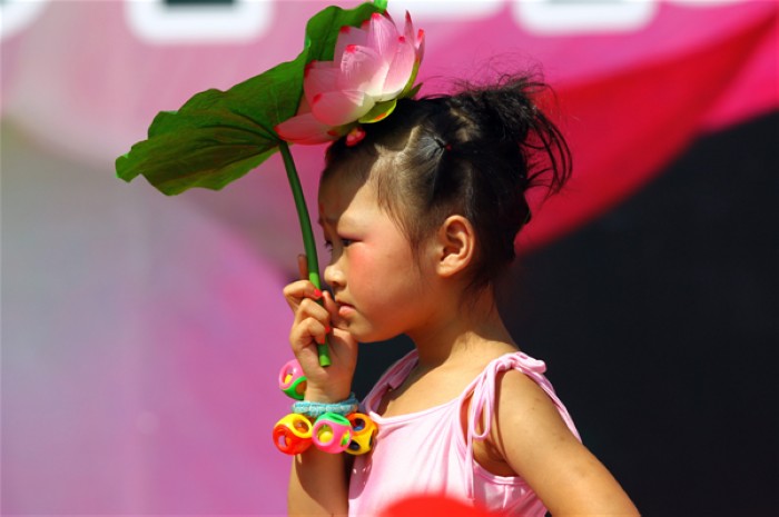 Un enfant cherche de l'ombre sous un lotus, lors de la première édition du Festival des Lotus à Wufu, dans la ville de Wuyishan, dans la Province du Fujian, en Chine de l'Est, le 26 juillet 2013. Le festival durera jusqu'au 1er octobre. [Photo Zouhong / Asianewsphoto]
