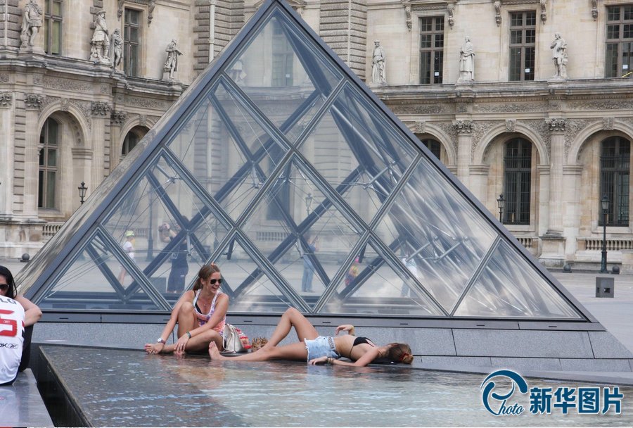 Le 19 juillet 2013, en proie à une vague de chaleur, de nombreux touristes se rafraîchissent autour de la fontaine devant le palais du Louvre.