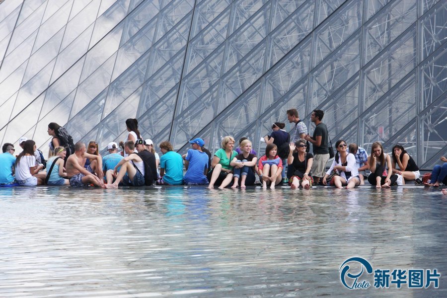 Le 19 juillet 2013, en proie à une vague de chaleur, de nombreux touristes se rafraîchissent autour de la fontaine devant le palais du Louvre.