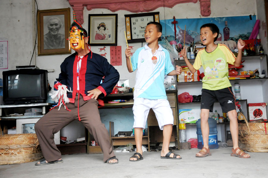 Le 18 août 2013, dans le district autonome Maonan de Huanjiang dans la province du Guangxi, Tan Shengci enseigne la danse Nuo à deux garçons, qui suivent chez lui une formation de la fabrication des masques de cette danse. (Photo : Xinhua)