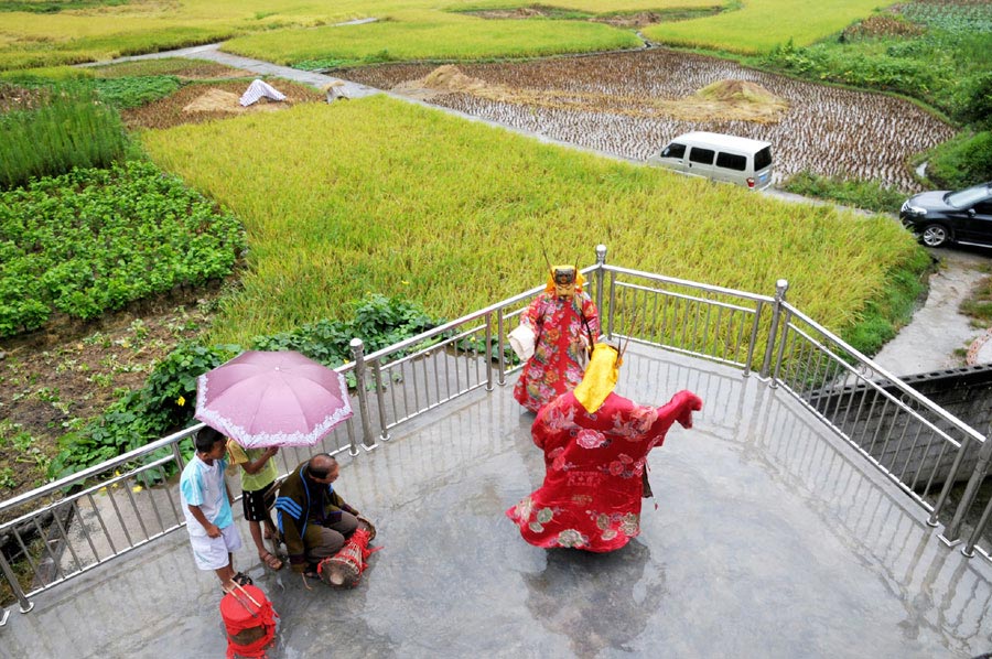 Le 18 août 2013, dans le district autonome Maonan de Huanjiang dans la province du Guangxi, Tan Shengci joue du tambour quand ses deux amis présentent un spectacle de la danse Nuo pour deux garçons, qui suivent chez de lui une formation de la fabrication des masques de la danse Nuo. (Photo : Xinhua)