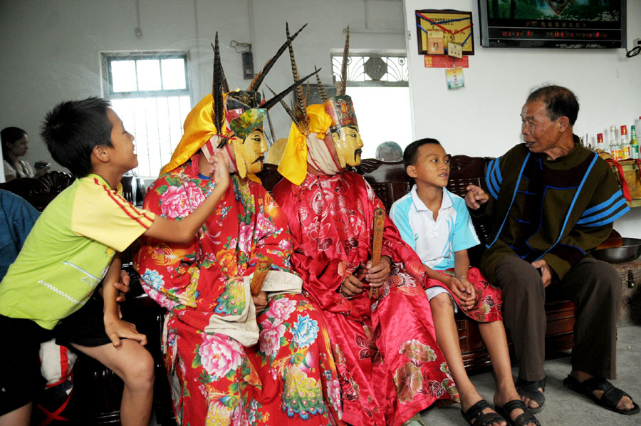 Le 18 août 2013, dans le district autonome Maonan de Huanjiang dans la province du Guangxi, Tan Shengci et deux amis racontent des histoires à deux jeunes concernant leur culture, qui suivent chez l'atisan une formation pour apprendre la fabrication des masques de la danse Nuo. (Photo : Xinhua)
