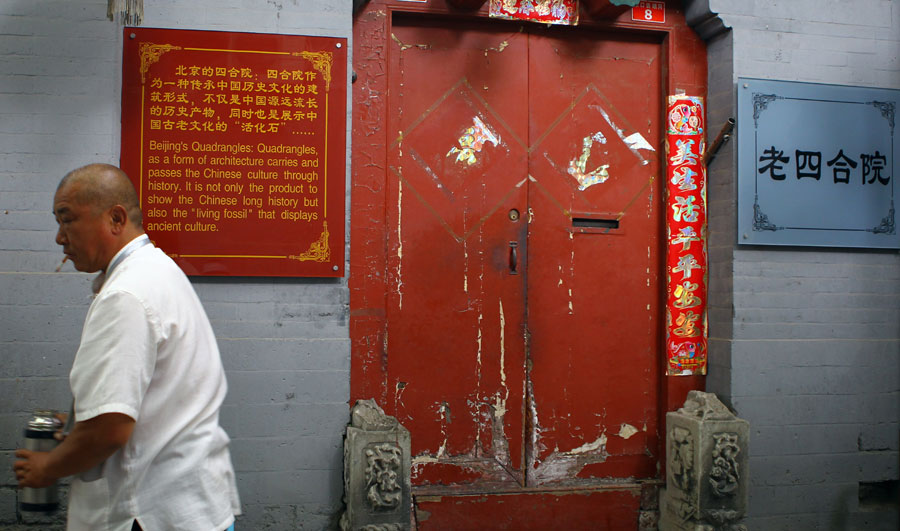 Un homme passe devant une porte de maison d'un hutong portant une pancarte racontant l'histoire des siheyuan de Beijing. [Photo Zou Hong / China Daily]