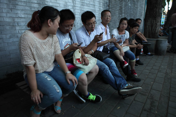 Des touristes jouent avec leur téléphone portable, lors d'une pause, dans une rue de Beijing, le 30 août 2013.