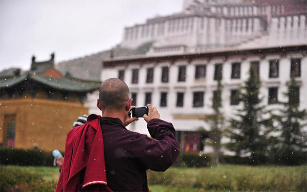 Un moine prend des photos du Palais du Potala sous la neige à Lhassa, capitale de la région autonome du Tibet, dans le sud de la Chine, le 28 octobre 2013. Des chutes de neige ont touché de nombreuses régions au Tibet lundi. [Photo/Xinhua ]