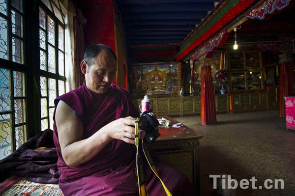 Un moine en robe pourpre consulte les photos d'un appareil numérique dans le monastère Drupeng au Tibet.