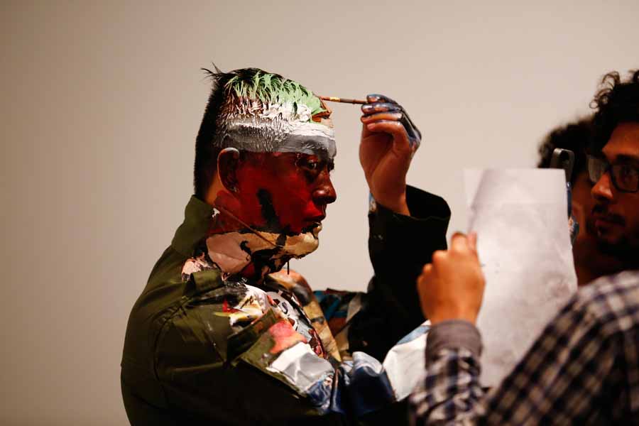 Liu Bolin, un artiste chinois, applique de la peinture sur son front alors qu'il se prépare à se fondre dans un décor, une étagère garnie de bandes dessinées, dans le cadre d’une série de spectacles à Caracas, le 2 novembre 2013