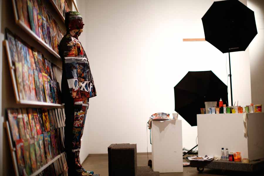 Liu Bolin, un artiste chinois qui utilise de la peinture appliquée sur son corps pour se camoufler, en face d'une étagère garnie de bandes dessinées dans le cadre d’une série de spectacles à Caracas, le 2 novembre 2013. [Photo / agences]