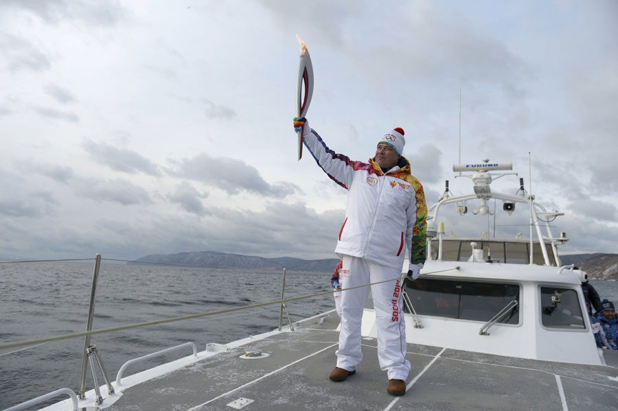 Un relayeur brandit la flamme des Jeux Olympiques d'hiver 2014 de Sotchi à bord d'un navire sur le lac Baïkal, document du Comité d'organisation de Sotchi 2014 publié le 23 novembre 2013.