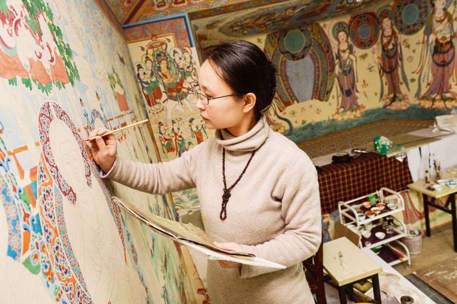 Yang Dongmiao dessine soigneusement les détails de peintures dans une grotte reconstituée à Xi'an, capitale de la Province du Shaanxi, dans le Nord-ouest de la Chine, le 10 décembre 2013. Yang Dongmiao et son mari Jin Weidong, ainsi que leurs quatre étudiants, reproduisent les peintures murales complètes des cavernes n° 45 et n° 220 des grottes de Mogao, un lieu inscrit au patrimoine mondial de l'UNESCO, dans la province du Gansu, au Nord-ouest de la Chine, depuis près de deux ans. Comme un grand nombre de peintures murales originales ont été gravement endommagées, ils ont dû reconstituer de nouvelles peintures après des recherches approfondies. Les deux grottes restaurées avec des peintures murales couvrant 300 mètres carrés seront bientôt présentées au public à Xi'an au début de 2014. [Photo / Xinhua]